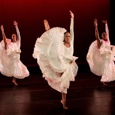 three women in white dresses are dancing on stage