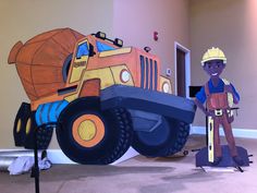 a boy standing next to a giant construction truck paper cutout on the floor in front of him