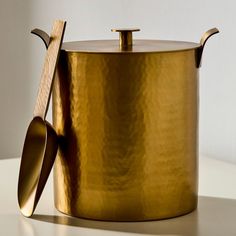 a gold pot with two spoons and a wooden spatula