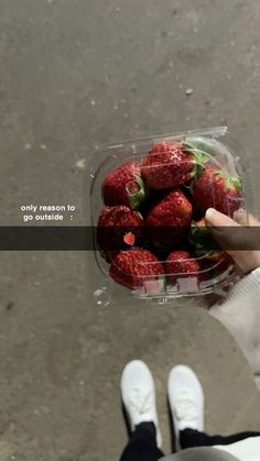 a person holding a plastic container full of strawberries with the words only reason to go outside