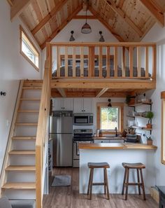 a kitchen and stairs in a tiny cabin style home with wood floors, white walls, and wooden ceilinging