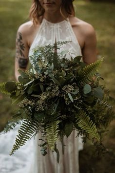 a woman in a white dress holding a bouquet of flowers and greenery on her wedding day