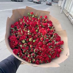 a person holding a bouquet of red roses on the sidewalk in front of some cars