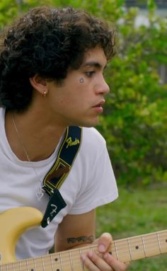 a young man with curly hair is playing an electric guitar in the grass and trees