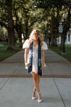 a woman walking down a sidewalk wearing a blue vest and white dress with her hands in her pockets