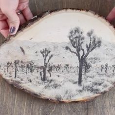 a person is holding a piece of wood with a painting on it that looks like a desert landscape