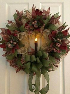 a wreath with a lit candle hanging on the front door, decorated with green and red ribbon