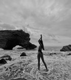 a woman standing on top of a sandy beach next to the ocean with her arms in the air