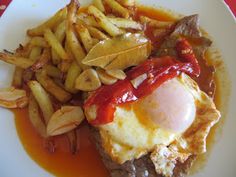 a white plate topped with french fries and an egg on top of meat covered in sauce