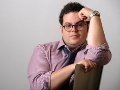 a man wearing glasses and a tie leaning on a chair with his hand on his head