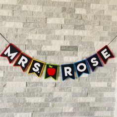 a sign that says mrs rose hanging from a string with an apple in the middle