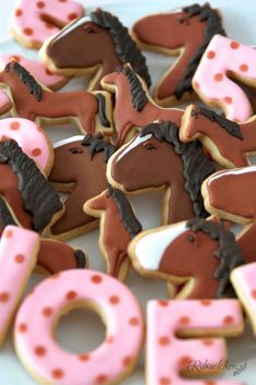 decorated cookies with horses and the word joy written in pink frosting on a white plate