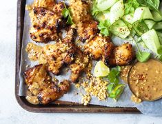 a tray filled with chicken, salad and dressing on top of a white tablecloth