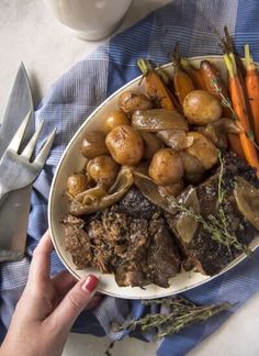 a plate full of roast, potatoes and carrots on a blue napkin with a fork