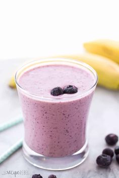 a smoothie in a glass with blueberries on the side and bananas next to it