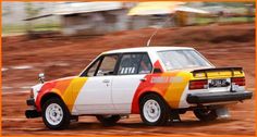 an orange, yellow and white car driving down a dirt road