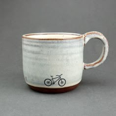 a white and brown coffee cup with a bicycle on the side, sitting on a gray surface