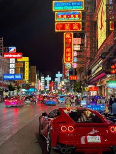 a red sports car driving down a city street at night with neon signs on the buildings