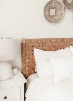 a bed with white linens and pillows in a bedroom next to two wicker baskets on the wall