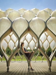 a woman is sitting on a bench in front of an intricately designed building with white panels