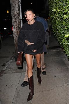 a woman walking down the street at night wearing boots and a black sweater with ripped knees