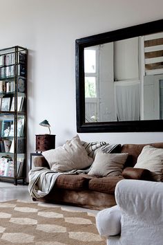 a living room with a couch, mirror and bookshelf on the wall in front of it