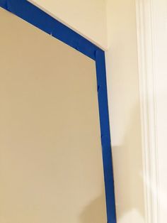 a mirror with blue tape on it in the corner of a room that is being painted