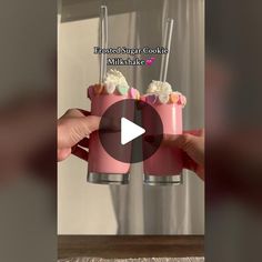 two pink cups with whipped cream and sprinkles on them are being held up