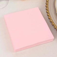 a pink paper sitting on top of a table next to a plate with gold trim