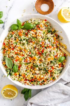 a white bowl filled with rice salad next to lemons and basil on a marble surface