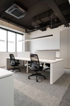 an empty office cubicle with white desks and black chairs