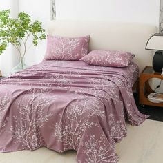 a bed with pink comforter and pillows on it in a room next to a plant