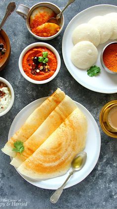 an assortment of food on plates with spoons and sauces around them, including pita bread