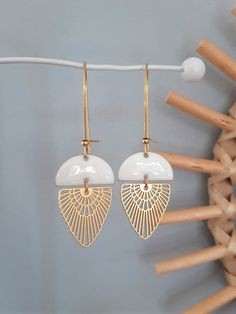 two pairs of white and gold earrings hanging from a hook on a clothes line in front of a wall