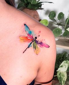 a colorful dragonfly tattoo on the back of a woman's shoulder