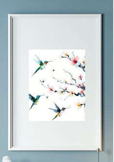 a white framed photograph with hummingbirds and flowers on the bottom right corner, against a blue wall