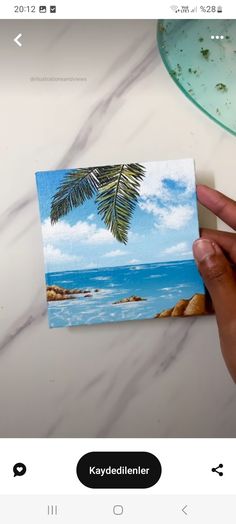 someone is holding up a card with a palm tree on the beach in the background