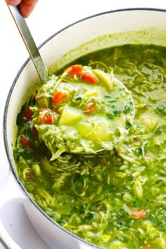 a ladle full of green soup being held by a person with a spoon in it