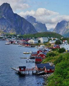 there are many small houses on the water by the shore and mountains in the background