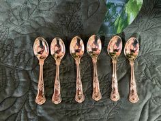 five antique spoons are lined up in a row on a green velvet surface with a leafy background