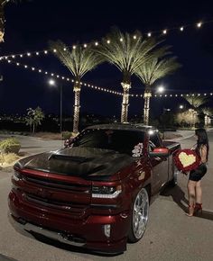 a woman standing next to a red truck with flowers in it's trunk and lights on