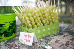 there are some grapes on sticks in a green basket next to a tin can and a sign that says garnish tails