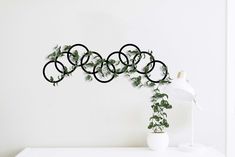 a white table topped with a vase filled with green plants and an iron ring wall decoration