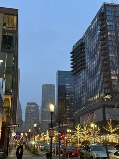 a city street filled with lots of traffic next to tall buildings and trees covered in christmas lights