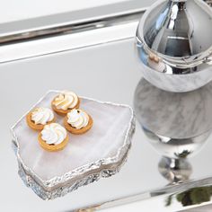 three small desserts are sitting on a silver platter next to a glass vase