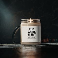 a candle sitting on top of a wooden table next to a black mug with the words the work scent written on it