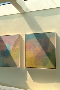 two paintings hanging on the side of a wall next to each other in front of a window