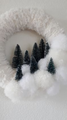 a white wreath with trees on it and fluffy snow around the edges, in front of a white wall