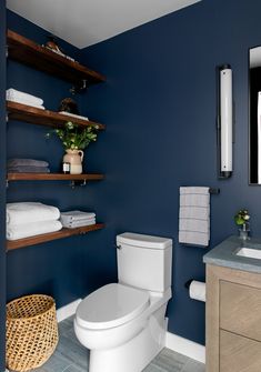 a white toilet sitting next to a wooden cabinet in a bathroom with blue walls and shelving