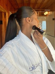 a woman is brushing her teeth in the bathroom while wearing a white robe and pearls